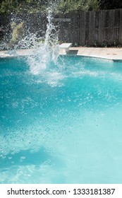 Guy Jumps Into An Outdoor Swimming Pool In The Summer. Man Lands In Pool From Jumping Off Diving Board Doing Cannon Ball Into A Pool With Big Splash As He Lands In The Deep End Of The Pool.