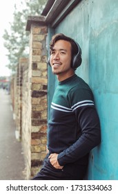 Guy leaning on a wall in the street, listening to music with headphones