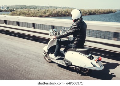 Guy In Leather Jacket And Helmet Is Riding On Scooter Through The City Bridge