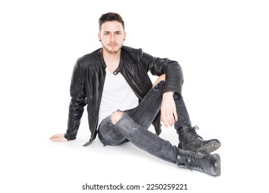 guy in leather jacket sit isolated on floor and look at camera in serious and pensive way while relax and chill unsmiling with arm on leg dressed in casual black