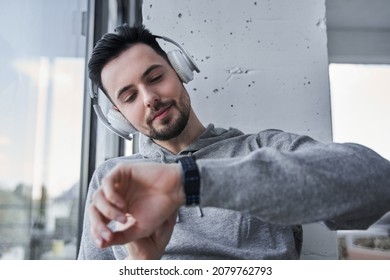 Guy looking time at his wristwatch while sitting near the window and listening music