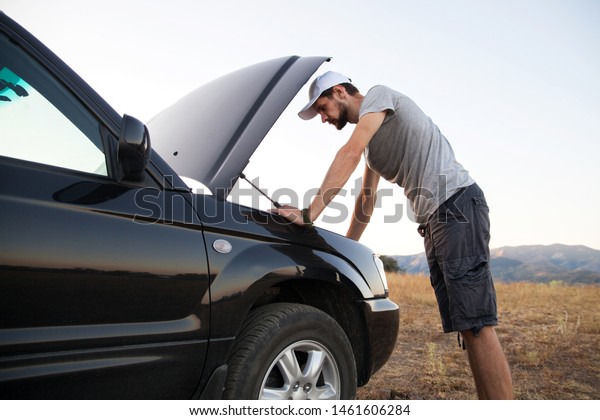 Guy opened the hood of the car\
and looks at the engine. Emergency stop and car repair en\
route