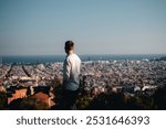 Guy overlooking city of Barcelona, standing with his back to the camera in white shirt, seeing horizon and the sea in the distance