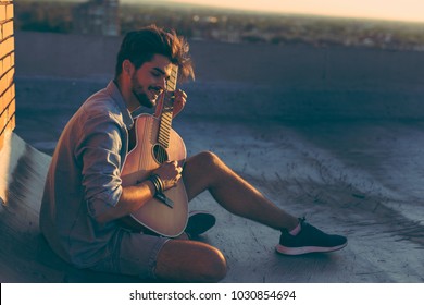 Guy playing the guitar on a building rooftop, relaxing and enjoying hot summer days
