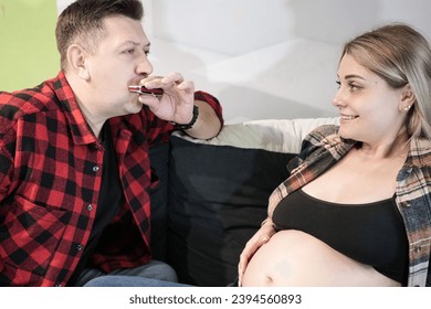 A guy plays the harmonica to a pregnant girl. Happy pregnant couple. A family is expecting a child. Conscious pregnancy concept - Shutterstock ID 2394560893