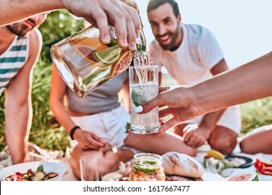 Guy pouring fresh homemade lemonade into glass of his girlfriend at outdoor party. People background. Close up view. Selective focus - Powered by Shutterstock