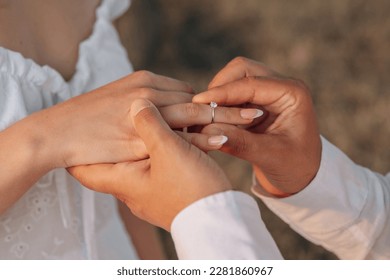 A guy puts a diamond engagement ring on his girlfriend's finger, close-up photo. An offer of a hand and a heart. Wedding ring - Shutterstock ID 2281860967