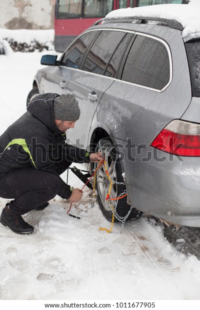 Guy putting the\
snow chains on his tires. 