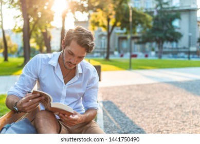 Guy reading book with text space. Young man reading book in park copy space. Man sitting on bench reading book in town. Happy positive guy reading book