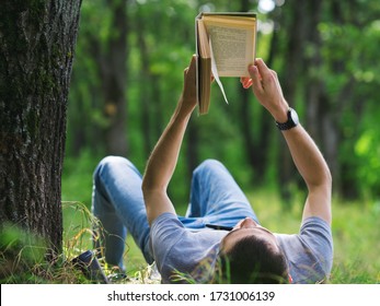 公園の限定フォーカスで緑の草の上に置かれた本を読む男