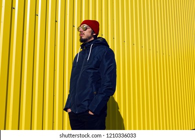 guy in the red hat stands at the wall of the iron house in nature next to the lake