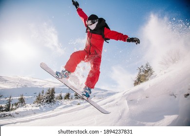 A Guy In A Red Jumpsuit Jumps On A Snowboard