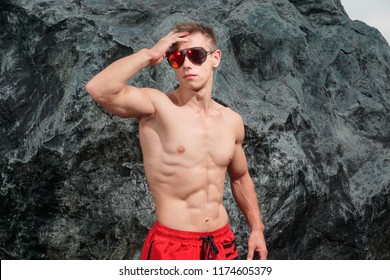 Guy In Red Shorts. Sexual Man  Fitness Model And Bodybuilder. Posing Chest And Six Pack Abs. Concept Of Power.