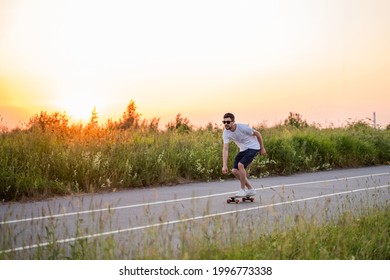 a guy rides a longboard skateboard on the road against the background of the sunset