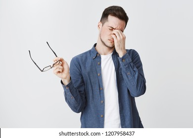 Guy Rubbing Eyes As Feeling Tired After Wearing Glasses While Working Over Freelance Project On Computer Standing With Eyewear In Hand And Closed Eyes Being Drained And Exhausted, Being Hardworking