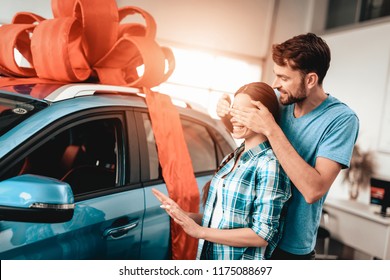 A Guy Shows A New Car To Girlfriend. Present Concept. Staring At Each Other. Automobile Salon. Make A Decision. Gift Ribbon. Eyes Closed. Good Offer. Happy Together. Successful Buying.