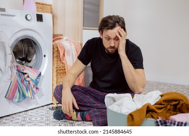 Guy sits on the laundry room floor with the washing machine open, throwing all the clothes into the drum, guy doesn't know how to do housework, face crumpled, catches head with hand. - Powered by Shutterstock