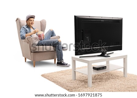 Guy sitting in an armchair watching television and eating popcorn isolated on white background