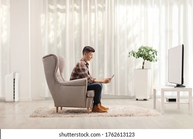 Guy Sitting At Home In An Armchair And Using A Mobile Phone In Front Of A Tv