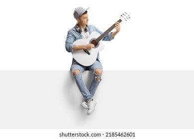 Guy sitting on a blank panel and playing an acoustic guitar isolated on white background - Powered by Shutterstock