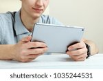 The guy is sitting at the table with a tablet on a neutral background. Close-up.