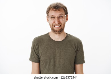 Guy Squinting And Making Funny Face Eating Sour Lemon Frowning And Wrinkling Nose Standing Disgusted And Dissatisfied Over White Background In Transparent Glasses And Green T-shirt