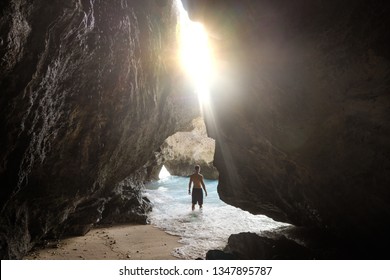 guy standing in the cave with a view of the waves of the ocean