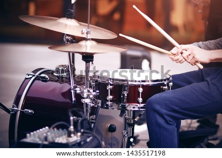 Guy is a street musician in blue pants playing rhythm on a beautiful red drum set with wooden drumsticks