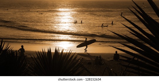 Guy With Surfboard Walking On A Beach At Sunset