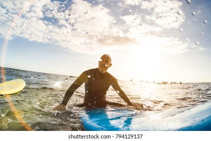 Guy surfer relaxing on surfboard at sunset in Tenerife with unrecognizable people at surf boards on background - Sport travel concept with shallow depth of field with drops on lens as composition