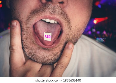 guy swallows puts a brand of narcotic acid on his tongue against background of a concert in a club. Junkies have fun at night on raver party at a nightclub. Close-up on junkie young man is taking LSD.