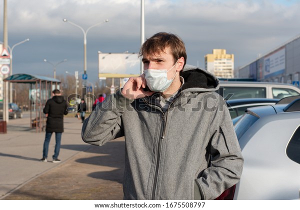 guy talking on a cell phone on the street. On the\
face a protective mask from coronavirus. Protection against\
bacteria and viruses transmitted by airborne droplets. passersby\
around. bus stop