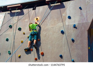 The Guy The Teenager Climbs To The Top Of The Artificial Rock, Is Engaged In Rock Climbing