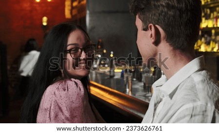 Guy tells funny anecdote to smiling lady. Brunette woman sincerely laughs at jokes and fixes hair. Positive atmosphere in subdued pub