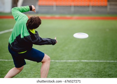 Guy throws and catches with flying disk at sports stadium. Concept is active and mobile in summer.