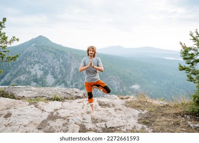 The guy trains the balance of the body standing on one leg on the edge of the cliff, the practice of balance, meditation in the mountains, the person keeps his balance. High quality photo - Shutterstock ID 2272661593