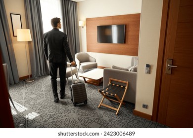 Guy with a travel suitcase stands in a hotel room - Powered by Shutterstock