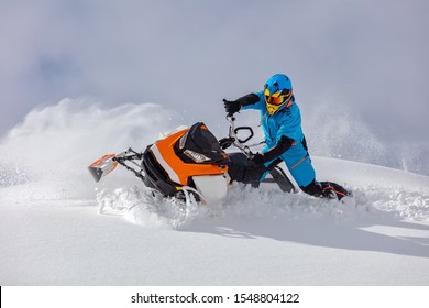 the guy turns a snowmobile in a mountain valley on the background of the clear snow and sky, leaving behind a trail of splashes. bright snow bike and suit without brands. Boondocker sports snowmobile - Shutterstock ID 1548804122