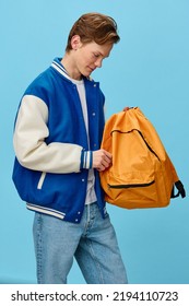 the guy unzips the orange backpack while standing on a blue background