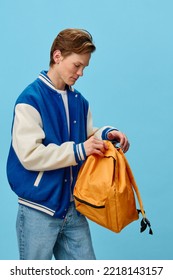 the guy unzips the orange backpack while standing on a blue background