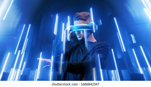 Guy using VR helmet scrolling invisible screen while interacting with virtual reality. Blue neon light. Augmented reality, future technology, game concept.