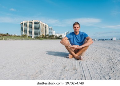 Guy walking along the empty sandy Miami beach. Happy handsome man tourist in casual clothes sitting on sandy beach. Travel and tourism concept.