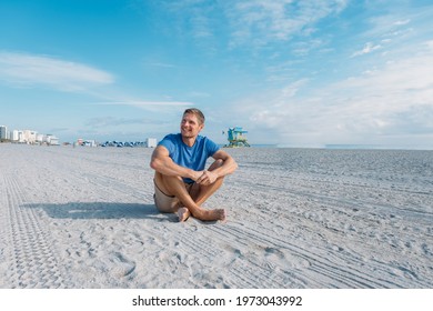 Guy walking along the empty sandy Miami beach.Happy handsome man tourist in casual clothes sitting on sandy beach. Travel and tourism concept.