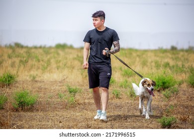 The Guy Walks The Dog On The Lawn In The Park. A Man Plays With A Pet On The Street. An Animal Welfare Volunteer Takes Care Of Homeless Animals At A Shelter. Kazakhstan, Almaty - June 20, 2022