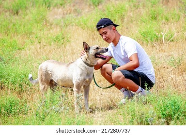 The Guy Walks The Dog On The Lawn In The Park. A Man Plays With A Pet On The Street. An Animal Welfare Volunteer Takes Care Of Homeless Animals At A Shelter. Kazakhstan, Almaty - June 20, 2022