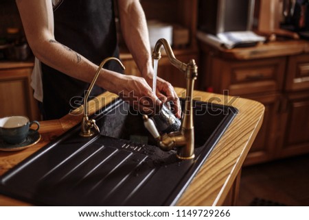a guy is washing the dishes in the kitchen with modern interior. close up side view photo