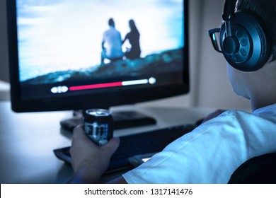 Guy Watching Movie Or Series Online From Streaming Service And Drinking Can Of Soda. Internet On Demand Video Player In Computer. Tv Show Episodes Marathon Late At Night. Young Man With Headphones.