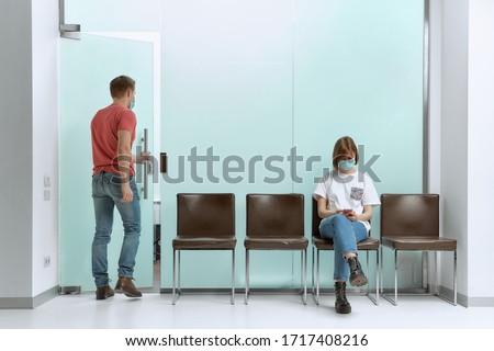Guy went to a doctor's appointment, and the girl sits in a queue and reads the news about the pandemic on her smartphone