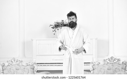 Guy In White Bathrobe Standing Between Two Antique Armchairs. Bearded Man Tightening His Robe. Sleepy Man Frowning In The Morning.