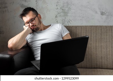 The Guy In The White Shirt Sitting On The Couch, Fell Asleep At Work On A Laptop. The Concept Of Laziness, Apathy, Frustration, Procrastination, The Person At Home. Copy Space.